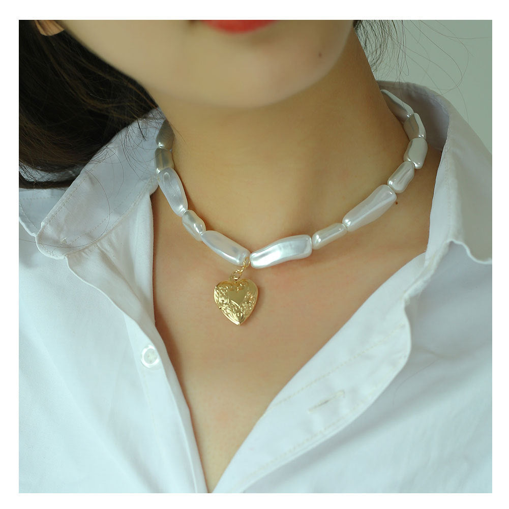 Pearl necklace with a gold heart pendant worn by a person in a white shirt.